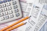 an array of tax forms with sharpened pencils and a calculator atop them